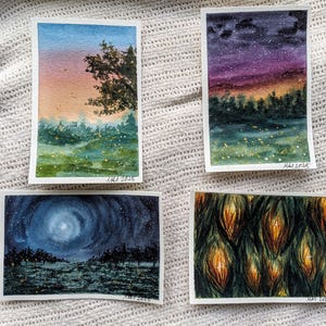 May include: Four watercolor paintings depicting landscapes. One shows a sunset with a tree, another a starry night, a third a moonlit scene, and the last an abstract pattern of glowing shapes. Each is signed "MAI 2025".