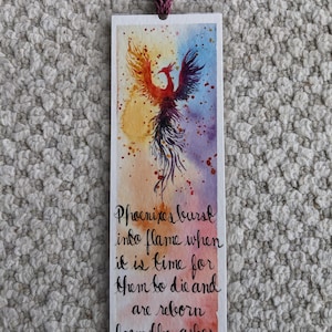 May include: A watercolor bookmark featuring a phoenix rising from flames with the quote "Phoenixes burst into flame when it is time for them to die and are reborn from the ashes." by J.K. Rowling from "Harry Potter and the Chamber of Secrets."
