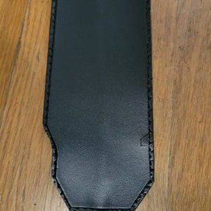 May include: A black shoulder strap pad with a smooth, rectangular surface and rounded corners. The pad features thick black stitching along the edges and is attached to a black nylon webbing strap with a silver-toned metal adjustment buckle.