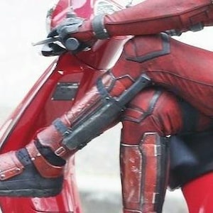 Puede incluir: Una persona con un traje de cuero rojo monta una scooter roja. El traje tiene detalles en negro y una funda con un objeto negro sujeto a la pierna. La persona lleva botas negras.