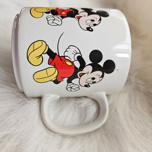 May include: White ceramic mug with a cartoon image of Mickey Mouse running. The mug has a handle and features two images of Mickey Mouse.