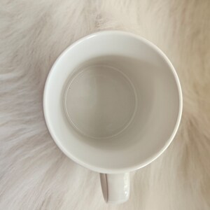 May include: White ceramic mug with a rounded handle. The mug is empty and ready to be filled with a hot beverage.