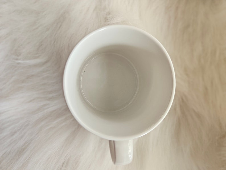 May include: White ceramic mug with a rounded handle. The mug is empty and ready to be filled with a hot beverage.