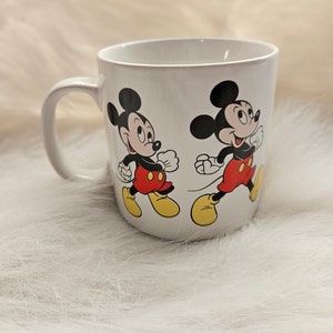 May include: White ceramic mug with a black and red Mickey Mouse design. The mug features two Mickey Mouse characters walking side-by-side.