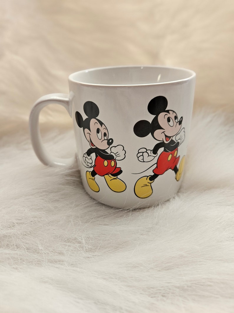 May include: White ceramic mug with a black and red Mickey Mouse design. The mug features two Mickey Mouse characters walking side-by-side.