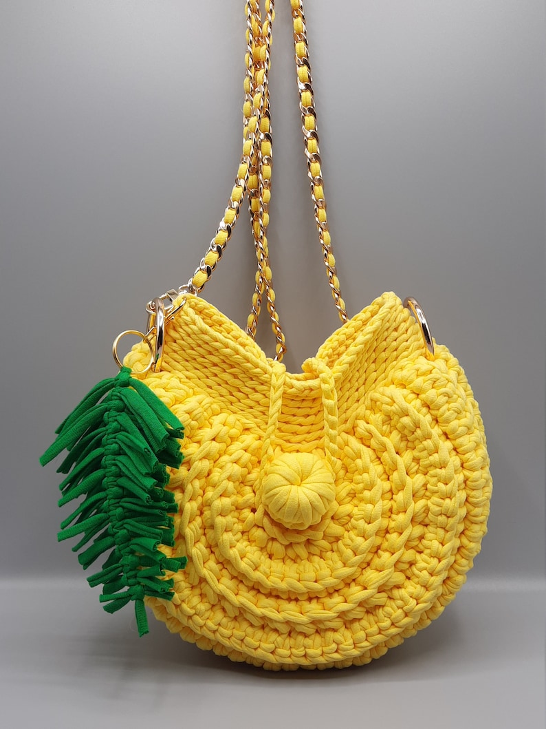 May include: A yellow crocheted handbag with a green tassel and a gold chain strap.