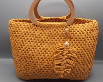 May include: A mustard yellow crocheted tote bag with wooden handles and a tassel charm.