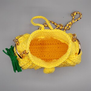 May include: A yellow crocheted pineapple-shaped handbag with a gold chain strap and green tassel.