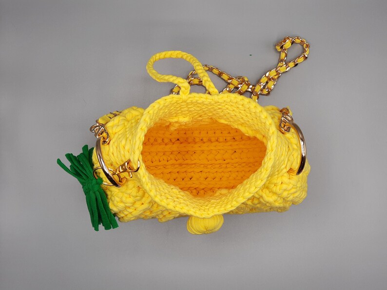 May include: A yellow crocheted pineapple-shaped handbag with a gold chain strap and green tassel.
