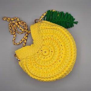 May include: A yellow crocheted handbag shaped like a lemon with a green crocheted leaf attached to the top. The bag has a gold chain strap.
