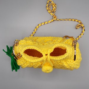 May include: A yellow crocheted handbag with a gold chain strap and a green felt pineapple top.