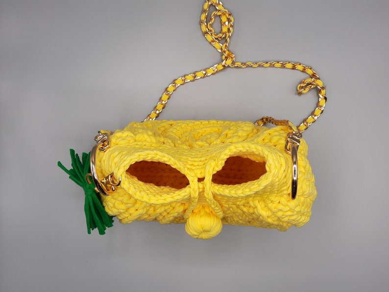 May include: A yellow crocheted handbag with a gold chain strap and a green felt pineapple top.