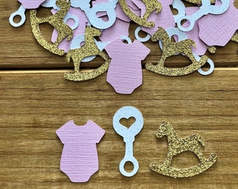May include: Pink and white paper confetti with gold glitter. The confetti features images of a baby onesie, a rocking horse, and a rattle.