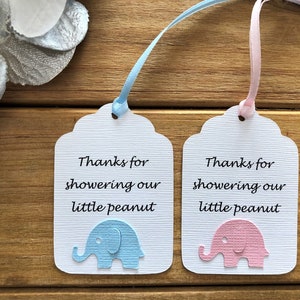 May include: Two white favor tags with blue and pink elephants and the text "Thanks for showering our little peanut".