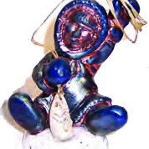 May include: A blue and white ceramic figurine of a person wearing a hooded parka and holding a fishing rod. The figurine is sitting on a white base.