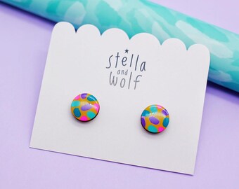 May include: A pair of colorful stud earrings with a yellow, pink, purple, and blue abstract pattern on a white card with the text "stella and wolf" in black.