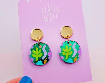 Puede incluir: Un par de pendientes verdes y dorados con un diseño abstracto colorido. Los pendientes están hechos de acrílico y tienen un poste dorado.