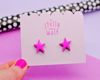 May include: A pair of pink star-shaped earrings on a white card with the text "Stella and Wolf" printed on it.
