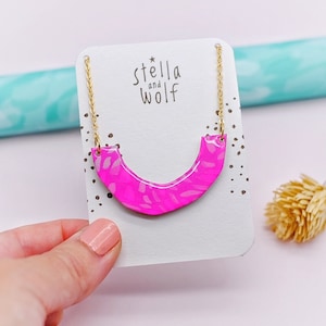 May include: A pink and white patterned necklace with a gold chain. The necklace is on a white card with the text "Stella and Wolf" printed on it.