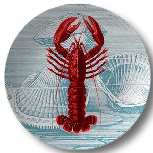 May include: A round ceramic plate featuring a vibrant red lobster illustration centered over a light blue background with detailed line-art drawings of various seashells and horizontal etched lines across the entire surface.