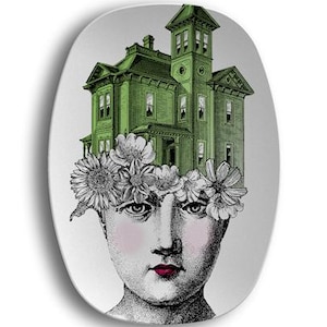 May include: Oval decorative plate featuring a woman's face with a green Victorian house in place of hair. The woman has a floral crown, pink cheeks, and red lips. The plate has a white background.