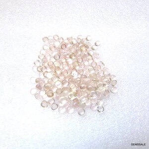 May include: A pile of small, round, translucent pink gemstones. The gemstones are smooth and have a slight shimmer.