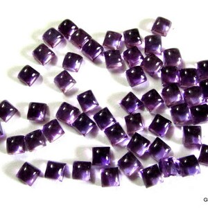 May include: A collection of purple square-shaped amethyst gemstones. The gemstones are faceted and have a shiny finish.