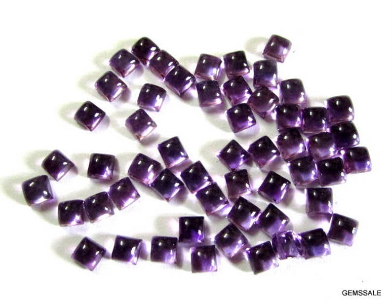 May include: A collection of purple amethyst gemstone cabochons, cut into square shapes. The stones are faceted and have a smooth, polished finish.