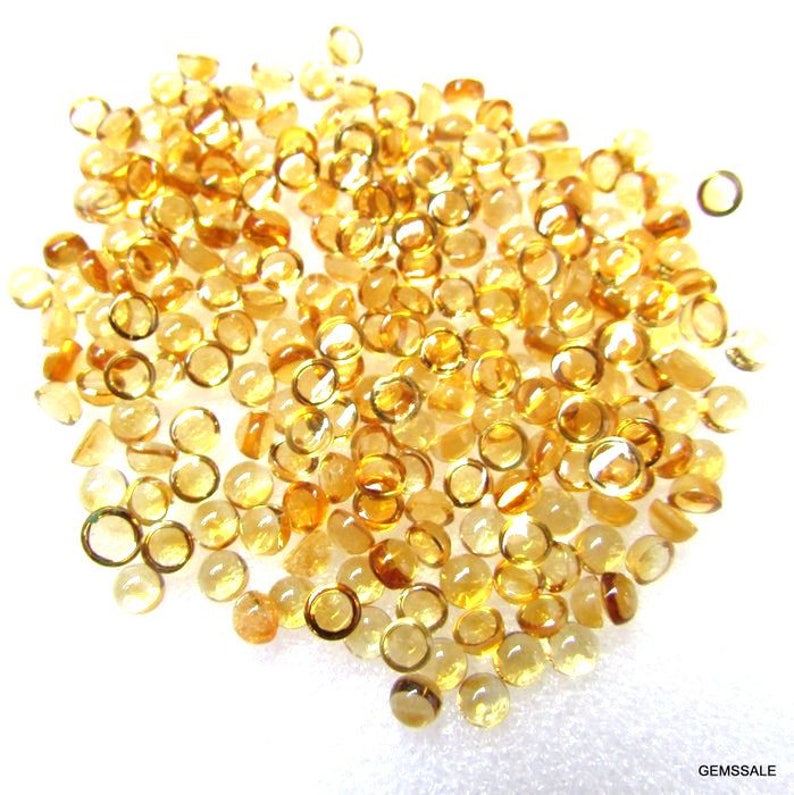 May include: A large pile of round, faceted, yellow gemstones. The gemstones are all approximately the same size and shape.
