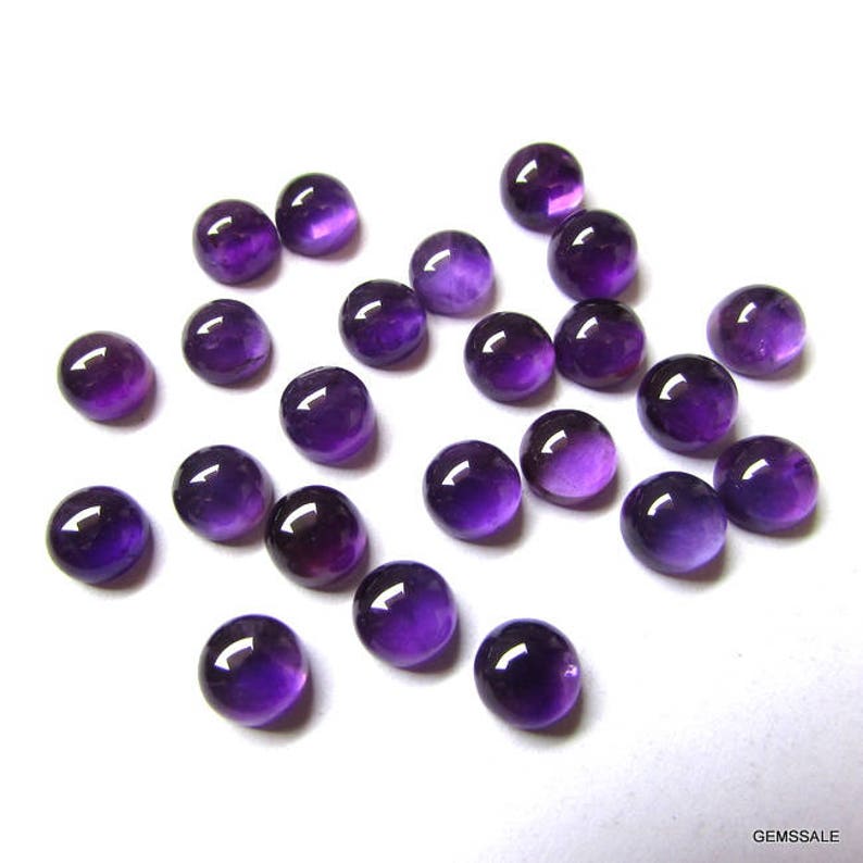 May include: A collection of 20 round, purple amethyst cabochons. The cabochons are smooth and polished, with a slight variation in size and shape.