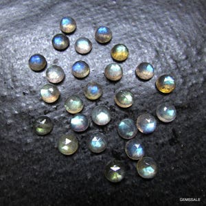 Puede incluir: Una colecci&oacute;n de 20 gemas de labradorita iridiscente, cada una con un patr&oacute;n &uacute;nico de matices azules, verdes y dorados. Las piedras son redondas y tienen un acabado liso y pulido.