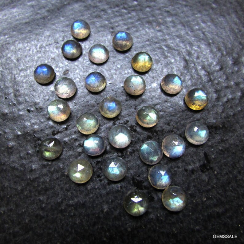 Puede incluir: Una colecci&oacute;n de 20 gemas de labradorita iridiscente, cada una con un patr&oacute;n &uacute;nico de matices azules, verdes y dorados. Las piedras son redondas y tienen un acabado liso y pulido.