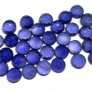 May include: A collection of 25 faceted round blue gemstones, each approximately 6mm in diameter. The stones have a light blue color and a smooth, polished finish.