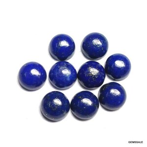 Pu&ograve; includere: Nove cabochon lucidati in lapislazzuli blu intenso, ciascuno con una forma arrotondata e bombata. Le pietre preziose sono disposte su uno sfondo bianco, mostrando il loro ricco colore e le inclusioni naturali. L'immagine &egrave; ben illuminata.