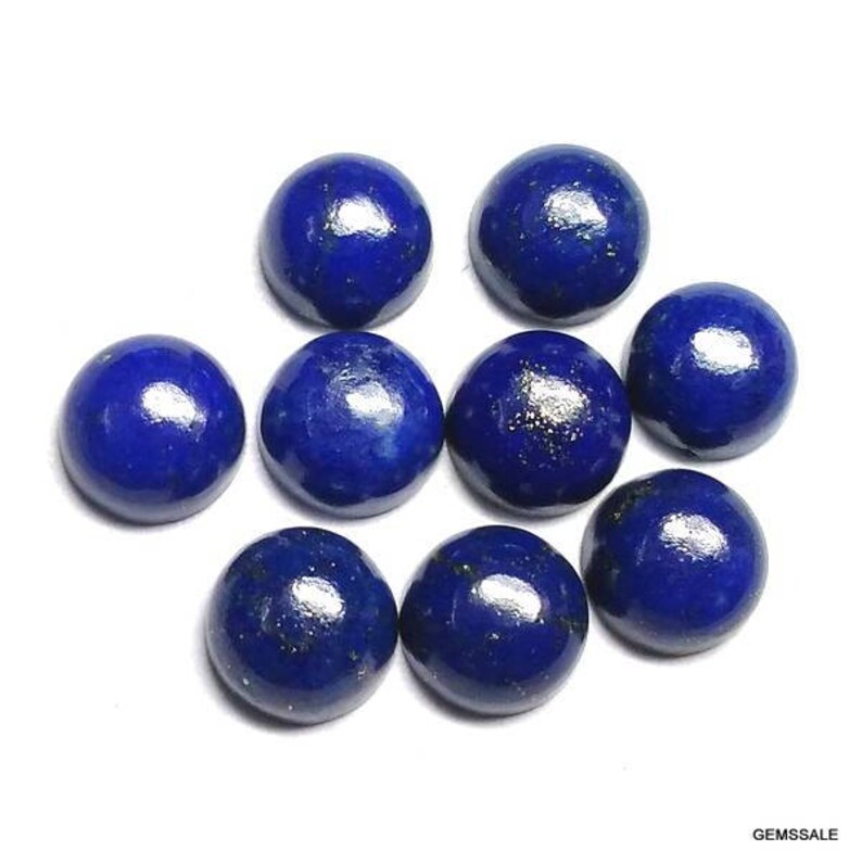 Pu&ograve; includere: Nove pietre preziose rotonde di lapislazzuli blu scuro lucido. Ogni pietra ha una superficie liscia e bombata con macchie d'oro. Le pietre preziose sono disposte su uno sfondo bianco, mostrando il loro ricco colore e la loro consistenza.