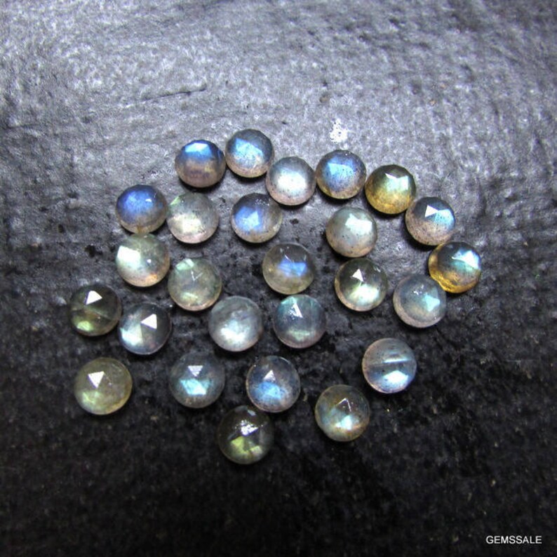 Puede incluir: Una colecci&oacute;n de 20 cabujones de piedras preciosas iridiscentes en varios tonos de azul, verde y gris. Las piedras son redondas y tienen un acabado liso y pulido.