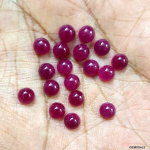 Op de afbeelding: Een verzameling ronde, robijnrode edelstenen, ongeveer 10 mm in diameter, getoond op een hand.