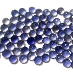 May include: A collection of round, faceted, purple gemstones. The stones are arranged in a loose pile, with some overlapping. The stones are all approximately the same size and shape.