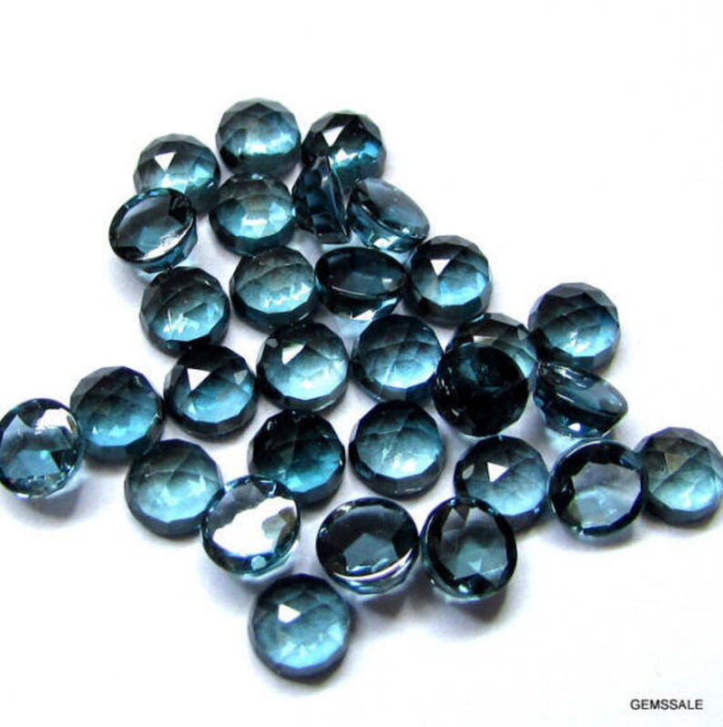 May include: A collection of 25 faceted, round, blue topaz gemstones. The stones are approximately 10mm in diameter and have a variety of shades of blue.