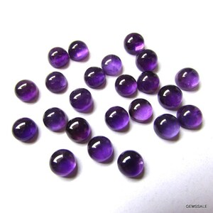May include: A collection of 20 round, purple amethyst cabochons. The cabochons are smooth and polished, with a slight variation in color and size.