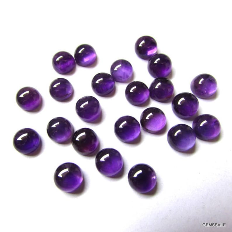 May include: A collection of 20 round, purple amethyst cabochons. The cabochons are smooth and polished, with a slight variation in color and size.