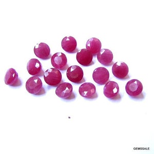 May include: A collection of 16 round, faceted ruby gemstones. The rubies are a deep pink color and have a smooth, polished finish.
