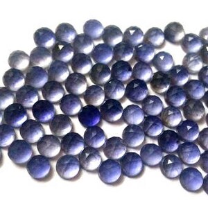 May include: A collection of round, faceted, purple gemstones. The gemstones are arranged in a loose pile and have a variety of shades of purple.