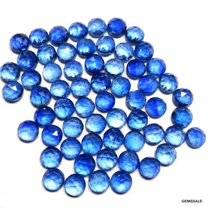 May include: A collection of round, faceted blue gemstones. The gemstones are arranged in a loose pile, with some overlapping. The gemstones are a deep blue color and have a shiny, polished finish.