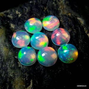 May include: A collection of eight iridescent opal cabochons, each displaying a unique blend of colors, including green, blue, pink, and orange.