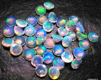 May include: A collection of iridescent opal gemstones in various shades of blue, green, and white. The gemstones are round and have a smooth, polished finish.