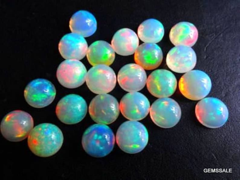 May include: A collection of round, iridescent opal cabochons. The opals are a mix of white, clear, and rainbow colors. The cabochons are approximately 6mm in diameter.