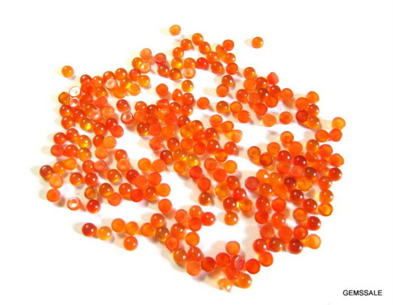 May include: A large group of small, round, orange carnelian cabochons. The cabochons are scattered on a white surface.