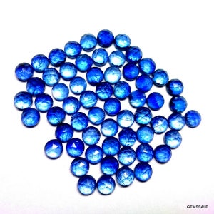 May include: A collection of round, faceted blue gemstones. The gemstones are arranged in a loose pile, with some overlapping. The gemstones are a deep blue color and have a shiny, reflective surface.