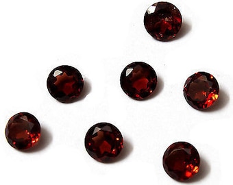 Pode incluir: Sete pedras preciosas redondas de cor vermelha com corte facetado. As pedras preciosas estão dispostas de forma dispersa sobre uma superfície branca.